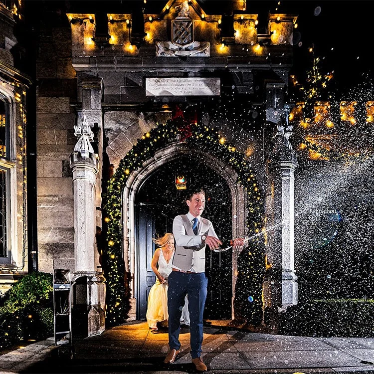 A groom sprays champagne under the arch at Clontarf Castle Wedding Venue in Dublin.