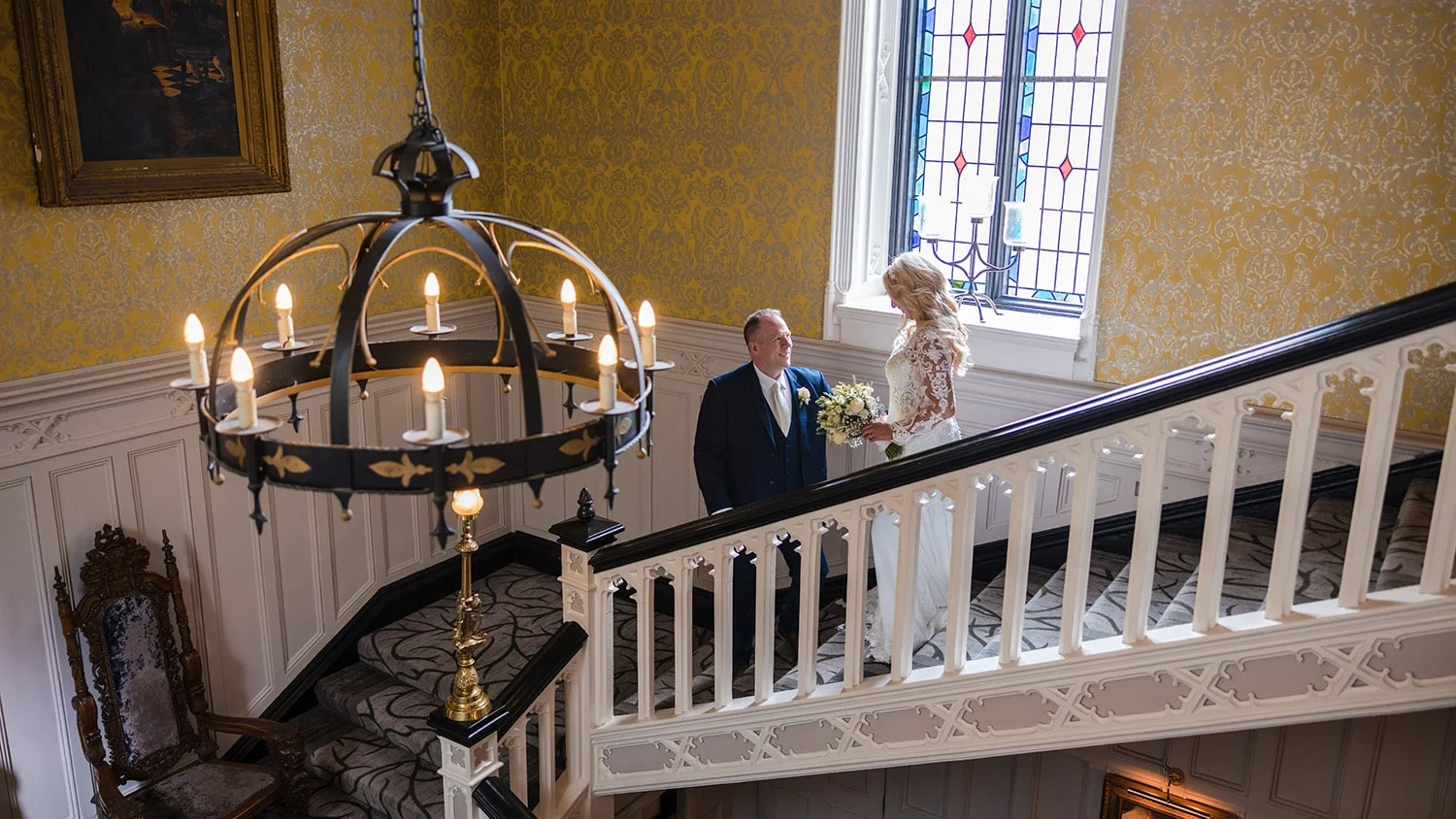 A man and woman look adorningly at each other on the grand stair case inside Clontarf Castle Hotel on their wedding day